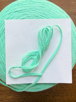 Load image into Gallery viewer, 100 Cotton Tape Cone Yarn in mint green color on wooden table, showcasing soft texture and ribbon-like structure.