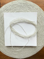 Load image into Gallery viewer, Maruyasu Techne 51 Paper 49 Modal Cone Yarn on a wooden table, showcasing its light color and smooth texture.
