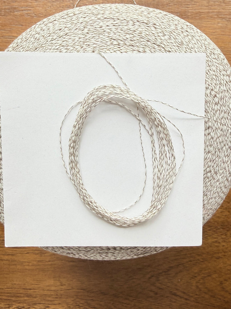 Ishikawa Safari Washi Blend Cone Yarn showcasing a soft white color in a cone shape on a wooden surface.