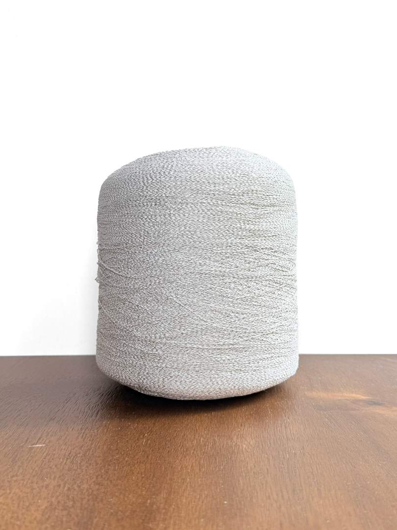 Ishikawa Safari Washi Blend Cone Yarn showcasing a soft white color in a cone shape on a wooden surface.
