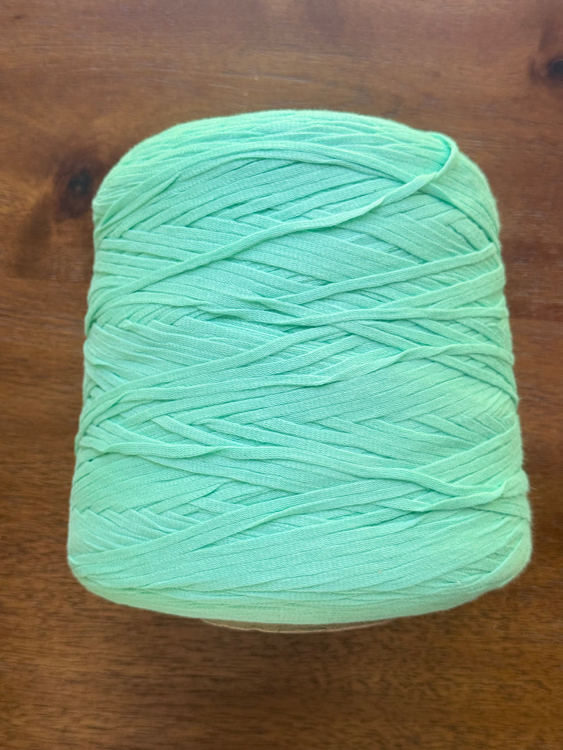 100 Cotton Tape Cone Yarn in mint green color on wooden table, showcasing soft texture and ribbon-like structure.