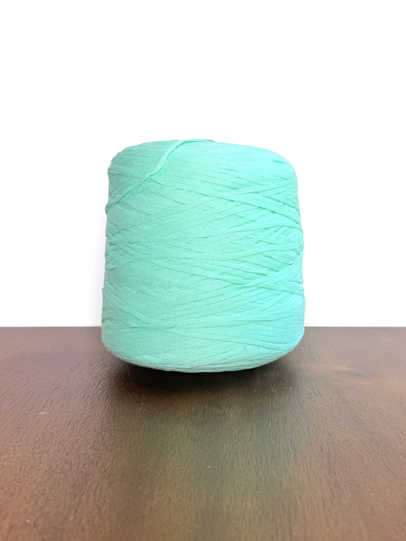 100 Cotton Tape Cone Yarn in mint green color on wooden table, showcasing soft texture and ribbon-like structure.