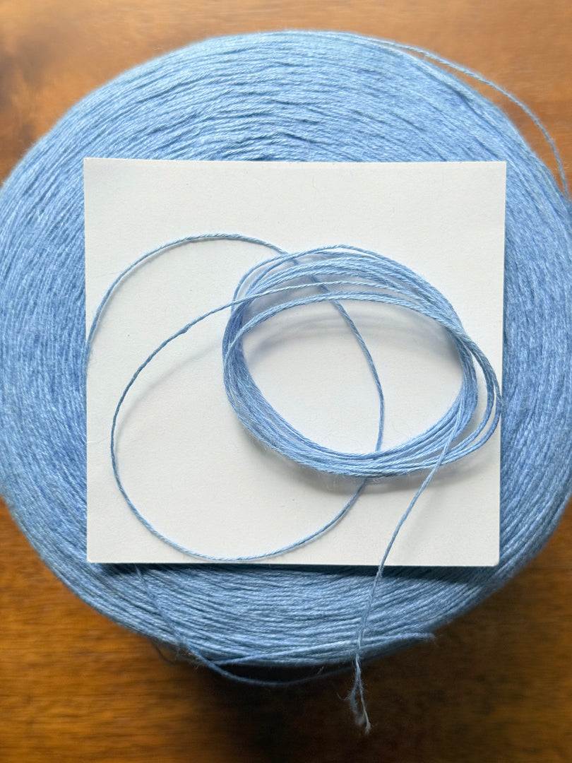 100 linen Cone Yarn in light blue color, showcasing the texture and structure of the yarn cone.