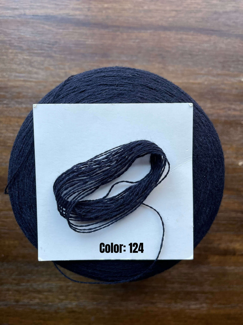 UPW 100 Extrafine Merino Wool cone yarn in color 124 on a wooden surface.